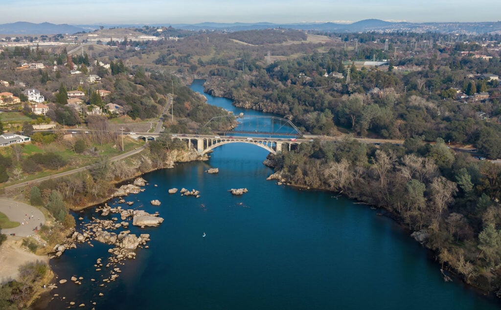 An aerial view of the Rainboow Bridge in Lake Natoma, Folsom, California, USA . Cars drive across the bridge, while a person paddleboards on the Lake